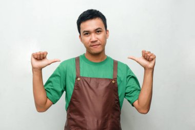 Yeşil tişörtlü ve kahverengi önlüklü gülümseyen genç adam iki başparmağıyla da kendisini işaret ediyor, arkadaş canlısı ve coşkulu bir ifadeyle. Kendini tanıtma ya da hizmet tanıtımı için ideal
