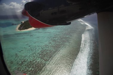 The view from the window of the seaplane on the tropical island and the wave of the surf in the coral reef. Romantic journey,  Travel destination