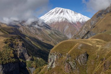 Karla kaplı dağ zirvesi renkli kayalık yamaçlar ve mavi gökyüzünün altında yeşil vadiler dağılmış bulutlarla panoramik manzaralı dağlık arazi ve engebeli seyahat turizm konsepti