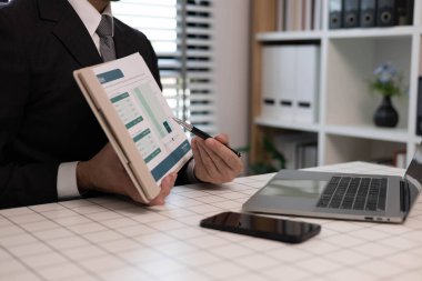 Bir adam elinde bir kitap ve bir kağıt parçasıyla masada oturuyor. O, bir kalemle kağıda yazıyor. Sahne, adamın yazılması gereken bir proje ya da görev üzerinde çalıştığını gösteriyor.