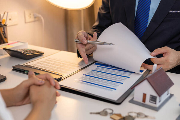 Мужчина указывает на лист бумаги, на котором написано "страховка". Он держит газету в руке и смотрит на нее.