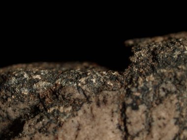 Koyu bir arka planda izole edilmiş pürüzlü granit taşın kenarına yakın plan. Görüntü karamsar, dramatik bir manzaraya sahip, sığ bir alan derinliği var..