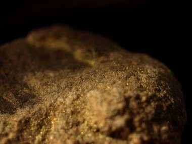 Engebeli bir kumtaşı mineral yüzeyinin makro çekimi, parlak altın detaylar ve yumuşak ışıklandırma ile, koyu bir arka plan üzerine kurulmuş.
