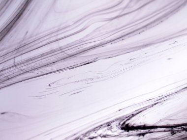 Sıvı siyah mürekkebin soyut yakın çekimi yoğun bir sıvıda kıvrılarak yumuşak, organik çizgiler ve açık mor arkaplanda mermer benzeri dokular oluşturur.. 