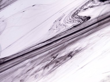 Sıvı siyah mürekkebin soyut yakın çekimi yoğun bir sıvıda kıvrılarak yumuşak, organik çizgiler ve açık mor arkaplanda mermer benzeri dokular oluşturur.. 