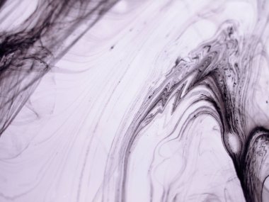 Sıvı siyah mürekkebin soyut yakın çekimi yoğun bir sıvıda kıvrılarak yumuşak, organik çizgiler ve açık mor arkaplanda mermer benzeri dokular oluşturur.. 