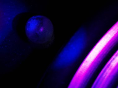 Küresel nesne, parlak, koyu bir arka plana karşı canlı pembe ve mavi ışıklarla yıkanarak soyut, kozmik bir atmosfer yaratıyor..