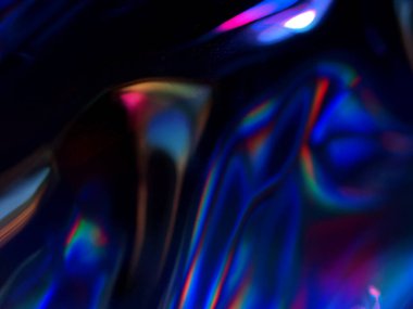 Renkli ışık yansımalarının soyut yakın çekimi. Görüntü, derinlik ve hareket hissi uyandıran canlı ve yanardöner renklere sahip koyu bir arkaplan içeriyor..