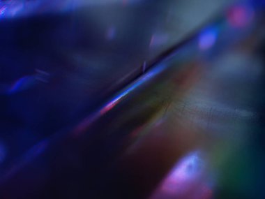 Renkli ışık yansımalarının soyut yakın çekimi. Görüntü, derinlik ve hareket hissi uyandıran canlı ve yanardöner renklere sahip koyu bir arkaplan içeriyor..