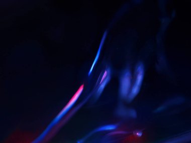 Renkli ışık yansımalarının soyut yakın çekimi. Görüntü, derinlik ve hareket hissi uyandıran canlı ve yanardöner renklere sahip koyu bir arkaplan içeriyor..