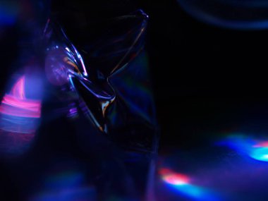 Renkli ışık yansımalarının soyut yakın çekimi. Görüntü, derinlik ve hareket hissi uyandıran canlı ve yanardöner renklere sahip koyu bir arkaplan içeriyor..