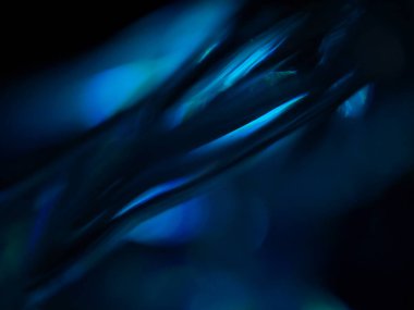 Renkli ışık yansımalarının soyut yakın çekimi. Görüntü, derinlik ve hareket hissi uyandıran canlı ve yanardöner renklere sahip koyu bir arkaplan içeriyor..