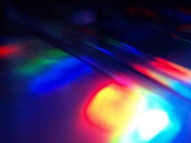 Renkli ışık yansımalarının soyut yakın çekimi. Görüntü, derinlik ve hareket hissi uyandıran canlı ve yanardöner renklere sahip koyu bir arkaplan içeriyor..