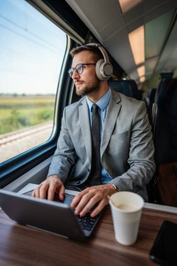 Hızlı trenle seyahat ederken dizüstü bilgisayarını kullanan orta yaşlı yakışıklı bir iş adamı. Modern ve hızlı seyahat kavramı.