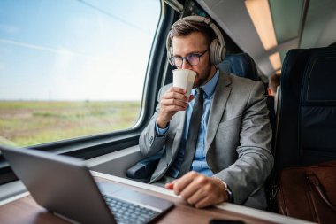 Hızlı trenle seyahat ederken dizüstü bilgisayarını kullanan orta yaşlı yakışıklı bir iş adamı. Modern ve hızlı seyahat kavramı.