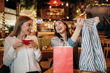 Alışveriş yaptıktan sonra kafeteryada ya da restoranda oturup mutlu mesut sohbet eden iki arkadaş. Ayrıca birbirlerine aldıkları kıyafetleri de gösteriyorlar..