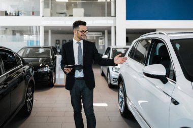 İyi görünümlü, neşeli ve samimi satıcı bir araba salonu veya showroom pozlar.