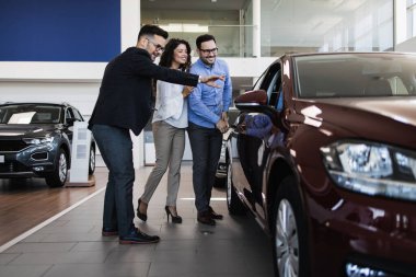 Araba galerisinden araba alan orta yaşlı bir çift. Araba satıcısı doğru karar vermelerine yardımcı oluyor..