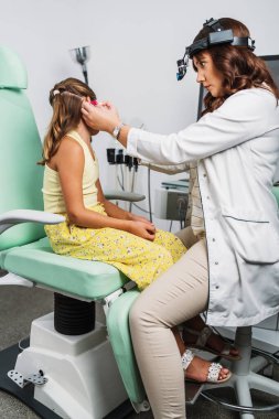 Female audiologist examining girl ear using otoscope in doctors office. Child receiving a ear exam. Nose and throat medical examination. Healthcare and medicine concept.