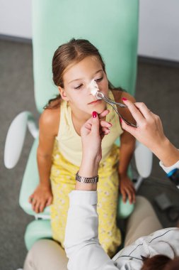 Female audiologist examining girl ear using otoscope in doctors office. Child receiving a ear exam. Nose and throat medical examination. Healthcare and medicine concept.
