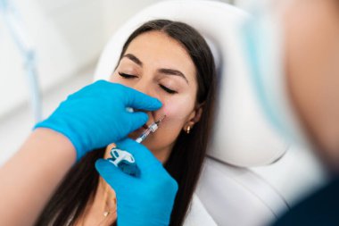 Güzellik uzmanı, kadının elmacık kemiklerine hyaluronik asit doldurucu yerleştiriyor. Hyaluronik asit doldurucu iğneyle ya da kanülle enjekte edilir. Yüz hatları konsepti.