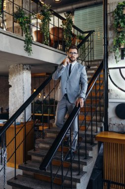 Yakışıklı ve gülümseyen orta yaşlı işadamı modern ofis veya kafe barında dururken akıllı telefonunu kullanıyor..