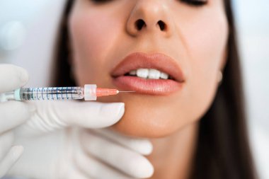 Çekici kadın güzellik kliniğinde gençleştirici yüz enjeksiyonu yaptırıyor. Güzellik uzmanı kadın kırışıklıklarını botulinyum toksin iğneleriyle ya da hyaluronik asit doldurucularıyla dolduruyor..