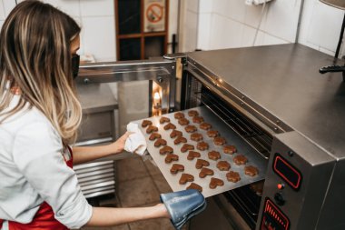 Koruyucu maskeli güzel bir bayan satıcı bir şekerleme dükkanında ya da fırında çalışıyor. O lezzetli tatlılar yapıyor. Coronavirus ve küçük işletme konsepti.
