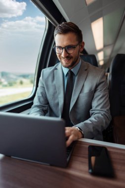 Hızlı trenle seyahat ederken dizüstü bilgisayarını kullanan orta yaşlı yakışıklı bir iş adamı. Modern ve hızlı seyahat kavramı.