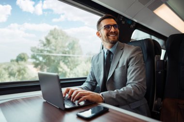 Hızlı trenle seyahat ederken dizüstü bilgisayarını kullanan orta yaşlı yakışıklı bir iş adamı. Modern ve hızlı seyahat kavramı.
