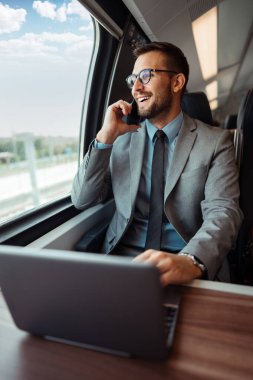 Hızlı trenle seyahat ederken dizüstü bilgisayarını kullanan orta yaşlı yakışıklı bir iş adamı. Modern ve hızlı seyahat kavramı.