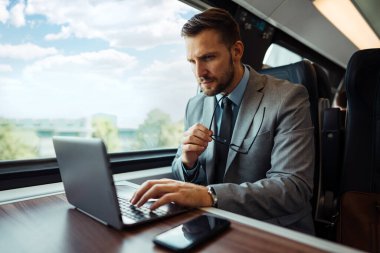 Hızlı trenle seyahat ederken dizüstü bilgisayarını kullanan orta yaşlı yakışıklı bir iş adamı. Modern ve hızlı seyahat kavramı.