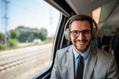 Yakışıklı iş adamı yüksek hızlı trenle seyahat ederken iyi vakit geçiriyor. Çevrimiçi iletişim, oyun ve eğlence için dizüstü bilgisayar ve kablosuz kulaklık kullanıyor.