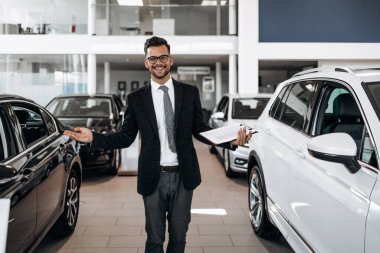 İyi görünümlü, neşeli ve samimi satıcı bir araba salonu veya showroom pozlar.