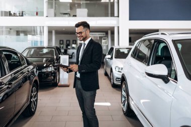 İyi görünümlü, neşeli ve samimi satıcı bir araba salonu veya showroom pozlar.