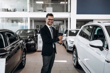 İyi görünümlü, neşeli ve samimi satıcı bir araba salonu veya showroom pozlar.