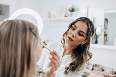Makyaj süreci. Makyaj için makyaj yapan profesyonel bir sanatçı. Güzellik uzmanının yüzüne odaklan. Parlak ışıklı güzellik salonu. 