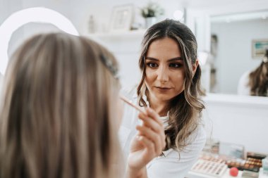 Makyaj süreci. Makyaj için makyaj yapan profesyonel bir sanatçı. Güzellik uzmanının yüzüne odaklan. Parlak ışıklı güzellik salonu. 