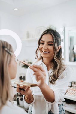 Makyaj süreci. Makyaj için makyaj yapan profesyonel bir sanatçı. Güzellik uzmanının yüzüne odaklan. Parlak ışıklı güzellik salonu. 