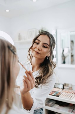 Makyaj süreci. Makyaj için makyaj yapan profesyonel bir sanatçı. Güzellik uzmanının yüzüne odaklan. Parlak ışıklı güzellik salonu. 