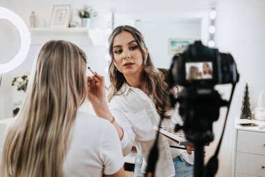 Evden ya da atölyeden güzel makyaj videosu yayınlayan mutlu genç bir kadın. Güzel çevrimiçi içerik kozmetikçisi makyaj yapıyor ve bazı iş araçlarını açıklıyor. Günlük kaydı ve çevrimiçi kanal çalışması. 