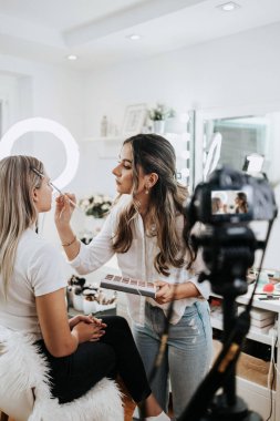 Evden ya da atölyeden güzel makyaj videosu yayınlayan mutlu genç bir kadın. Güzel çevrimiçi içerik kozmetikçisi makyaj yapıyor ve bazı iş araçlarını açıklıyor. Günlük kaydı ve çevrimiçi kanal çalışması. 