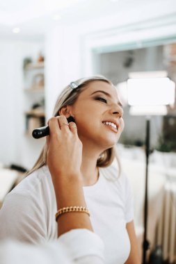 Makyaj süreci. Maket yüzünü fırçalayan profesyonel bir makyöz. Yüz temeli ve tonu cilde uygulanıyor. Güzellik salonundaki güzel sarışın kadının portresini yakından çek.. 