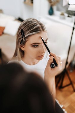 Makyaj süreci. Maket yüzünü fırçalayan profesyonel bir makyöz. Yüz temeli ve tonu cilde uygulanıyor. Güzellik salonundaki güzel sarışın kadının portresini yakından çek.. 