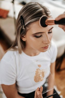 Makyaj süreci. Maket yüzünü fırçalayan profesyonel bir makyöz. Yüz temeli ve tonu cilde uygulanıyor. Güzellik salonundaki güzel sarışın kadının portresini yakından çek.. 