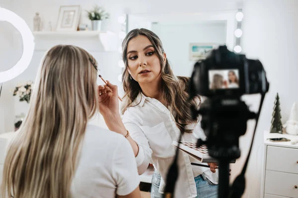 Evden ya da atölyeden güzel makyaj videosu yayınlayan mutlu genç bir kadın. Güzel çevrimiçi içerik kozmetikçisi makyaj yapıyor ve bazı iş araçlarını açıklıyor. Günlük kaydı ve çevrimiçi kanal çalışması. 