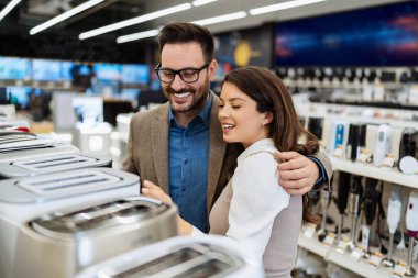 Beautiful and happy middle age couple buying consumer tech products in modern home tech store. They are choosing small kitchen appliances. People and consumerism concept.