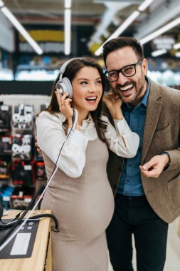 Beautiful and happy middle age couple buying consumer tech products in modern home electronics store. They are choosing high quality hifi audio speakers and audiophiles headphones. 