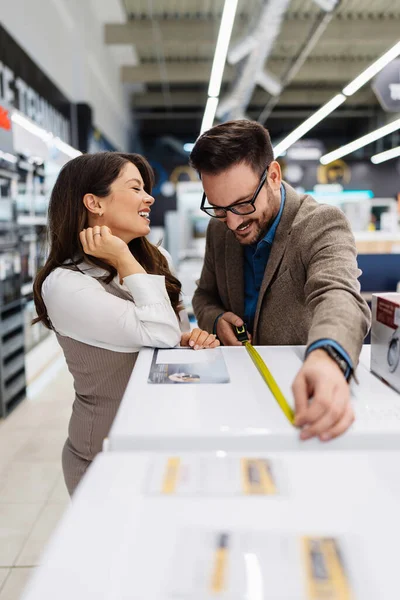 Beautiful and happy middle age couple buying consumer tech products in modern home appliances store. They are choosing washing or cloth dryer machine. People and consumerism concept.