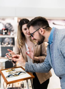 Zarif orta yaşlı işadamı yeni pahalı saatini seçip alıyor. Güzel, genç bir bayan satıcı iyi bir karar vermesine yardımcı olur. Moda tarzı ve zarafet konsepti.